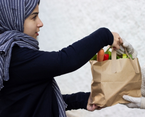 Muslimische junge Frau übergibt Lebensmitteltüte an Bedürftige, MEA Muslimische Ehrenamtsagentur Infoveranstaltung April